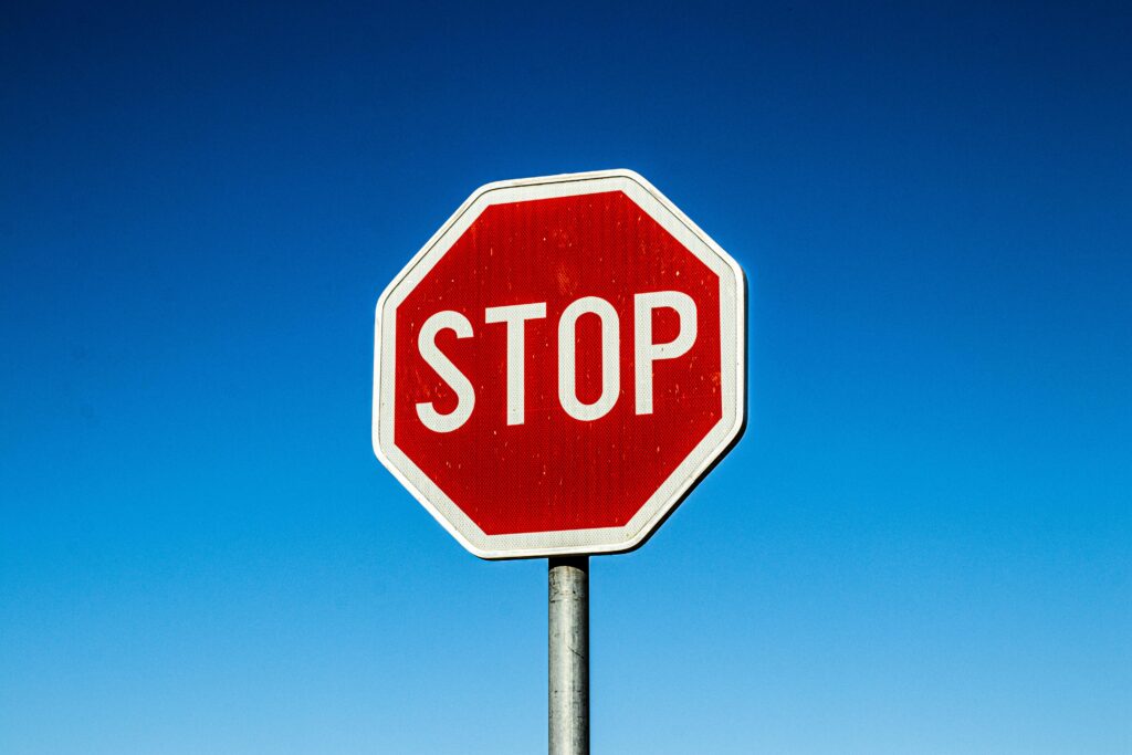 Red stop sign with bold white text against a clear blue sky for traffic regulation.